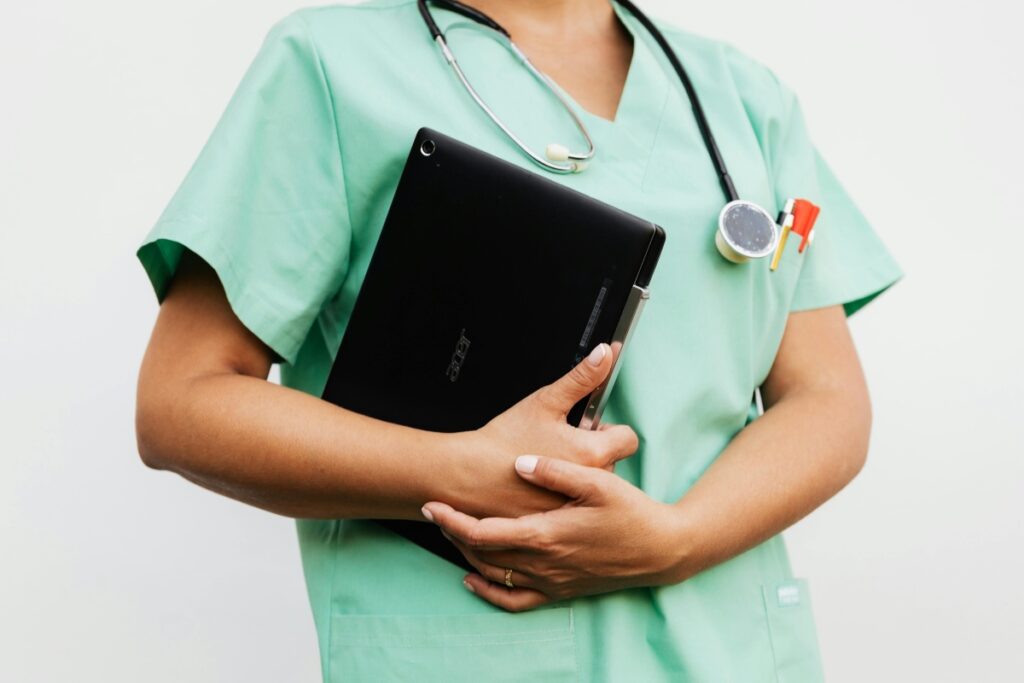 A nurse in green scrubs, holding a tablet.